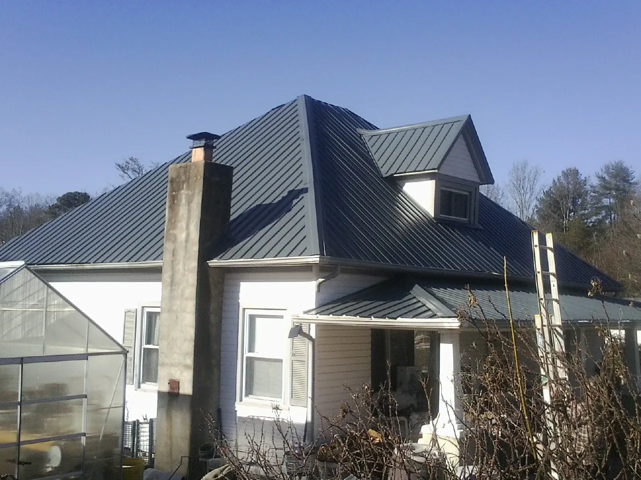 Dark blue standing seam metal roof on a white farmhouse with dormer — Slate & Tile Roof Repair by Roofing Brothers in Almo