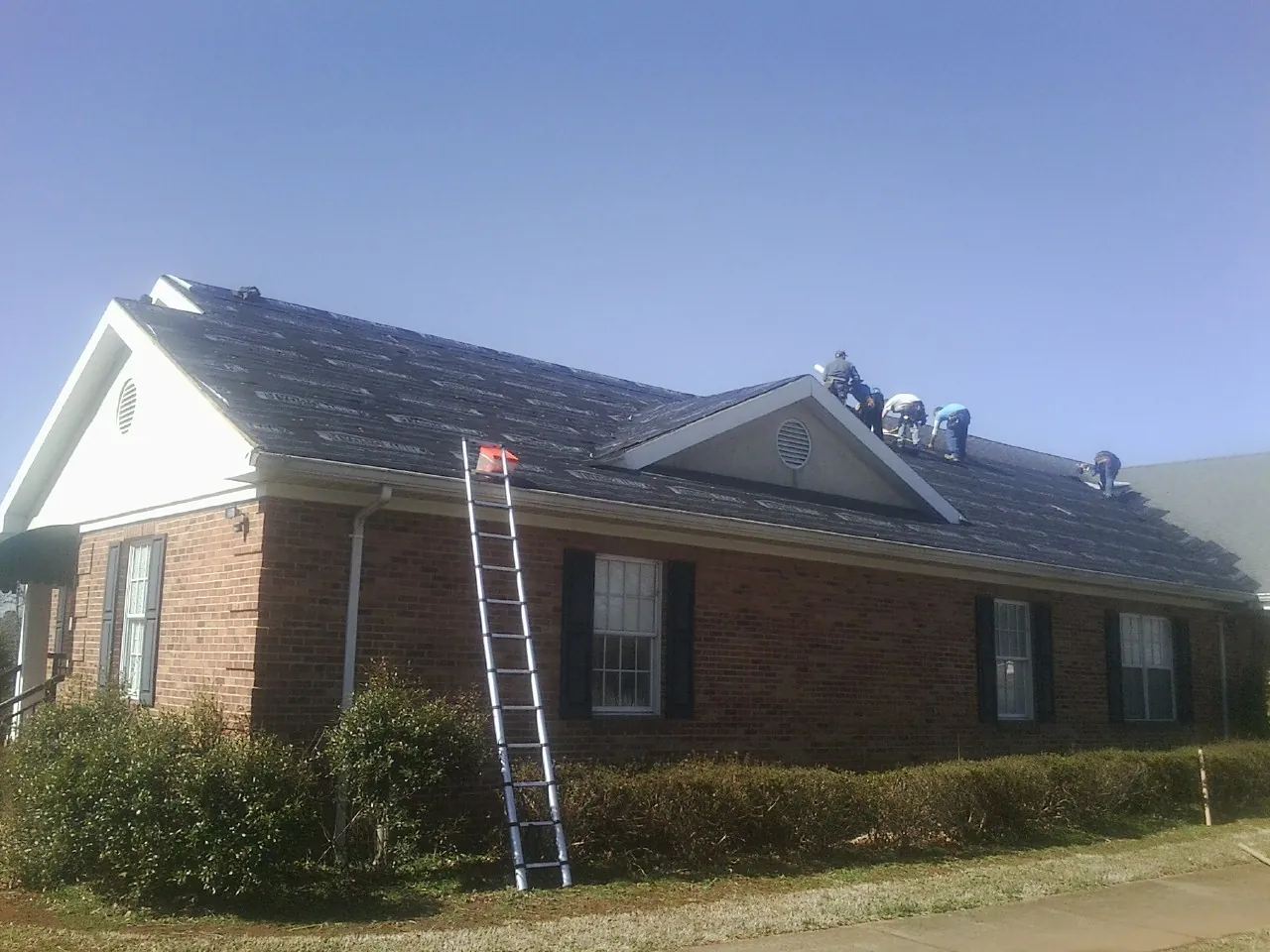 Crew tearing shingles off a brick ranch roof with a ladder set — Emergency Roof Repair work by our crew in Almo