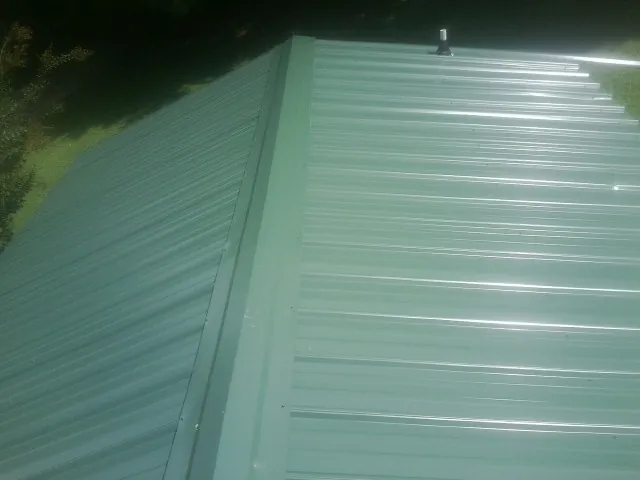 New green metal panels meeting at the ridge of a roof — Flat Roof Repair work by our crew in Almo