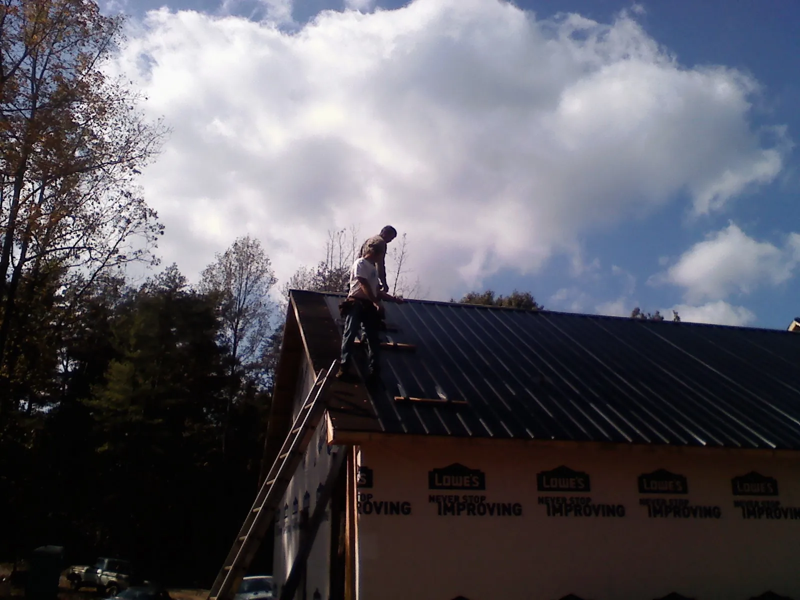 Roofer fastening dark metal panels high against a cloudy sky, from a Roof Inspection job in Almo
